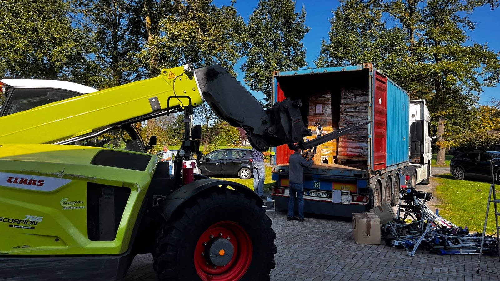 Ein grüner Teleskoplader schiebt eine Palette in den offenen Container, zwei Helfer packen mit an.