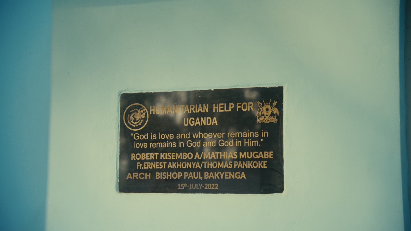 Gedenktafel mit der Aufschrift „Humanitarian Help for Uganda“ und den Namen Robert Kisembo, Mathias Mugabe, Fr. Ernest Akhonya, Thomas Pankoke und Erzbischof Paul Bakyenga, datiert 15. Juli 2022.
